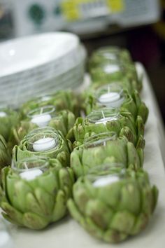 several jars filled with green artichokes sitting on a table next to plates