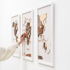 a woman is pointing at the world map on a white wall with three framed pictures