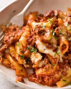 a white bowl filled with pasta covered in sauce and cheese, topped with parsley