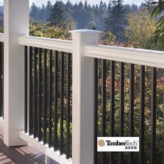 a white railing with black rails on a deck in front of some trees and bushes