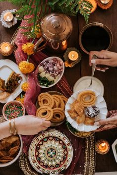 people holding plates with food on them at a table filled with candles and other foods