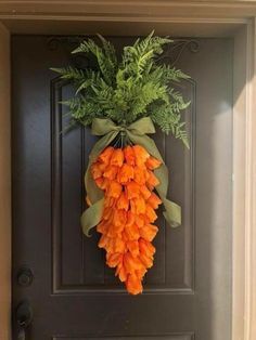 an orange carrot hanging on the front door with green leaves and greenery in it