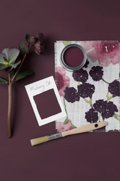 a purple flower and some paint next to a brush on a napkin with a tag