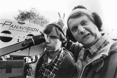 two people standing next to each other in front of a microphone and an airplane on the ground