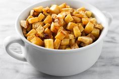 a white bowl filled with cooked potatoes on top of a marble countertop next to a knife