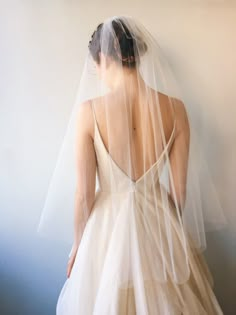 the back of a bride's wedding dress with a veil on her head and shoulders