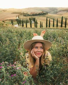 a woman wearing a hat laying in the middle of a field with her hands on her head