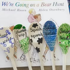 five wooden spoons with different designs on them sitting in front of a sign that says we're going on a bear hunt