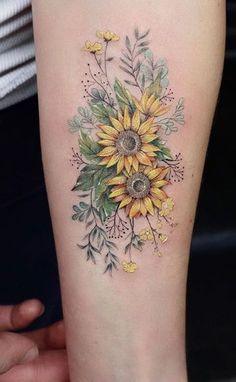 a sunflower tattoo on the arm with yellow flowers and green leaves in front of it