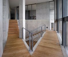 an empty room with wooden floors and stairs leading up to the second floor, in front of a concrete wall