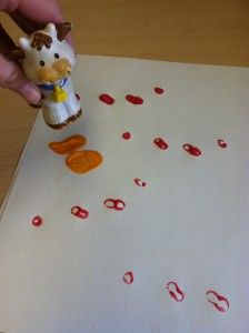 a hand is holding a small toy cow in front of a piece of paper with red dots on it