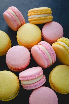 there are many different colored macaroons on the table and one is pink, yellow, and white