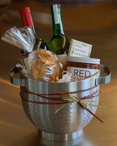 a silver colander filled with lots of food and wine bottles on top of a wooden table