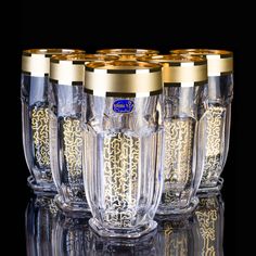 six glasses with gold rims are lined up in a row on a reflective surface