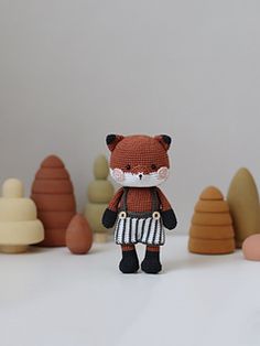 a knitted fox is standing in front of small trees and rocks, with one hand on his hip