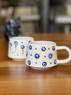 two white cups with blue designs on them sitting on a wooden counter top next to each other