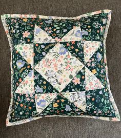 a green and white pillow with flowers on the front, sitting on a gray couch