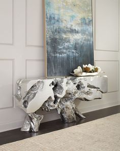 a painting is on the wall next to a table with silver leafy branches in front of it