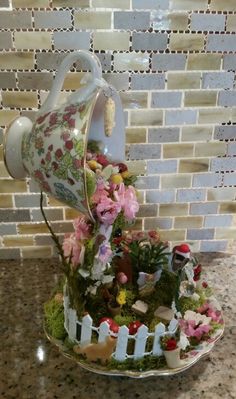 a teapot with flowers and plants in it sitting on a table next to a brick wall