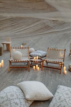 candles are lit in front of chairs and pillows on the ground with rocks around them