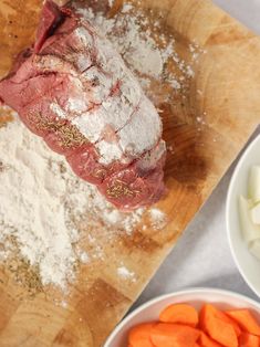 meat and vegetables on a cutting board next to flour, carrots, and garlic