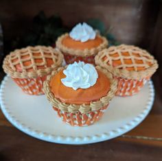 four cupcakes on a white plate with orange icing and whipped cream topping