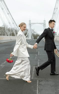 a man and woman holding hands while walking across a bridge with roses in their hand