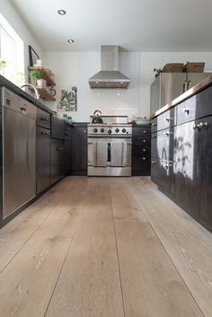 a kitchen with stainless steel appliances and wood flooring, along with an oven in the center