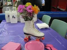 a purple table topped with pink and white roller skates next to a bouquet of flowers