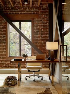 an office with a desk, chair and lamp in front of a large brick wall