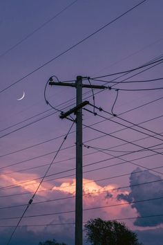 an electric pole with power lines in the foreground and a crescent moon in the background