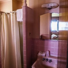 a bathroom with a sink, mirror and shower curtain in pink tiled wallpapered walls