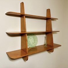 a wooden shelf with two glass vases and a green plate on the bottom, in front of a white wall