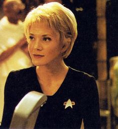 a woman with blonde hair wearing a star trek uniform and looking off into the distance