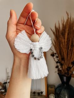 a hand holding a small white angel ornament with beads and tassels