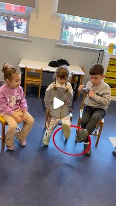 three children sitting on chairs in a classroom with one holding a bat and the other playing with a hula hoop