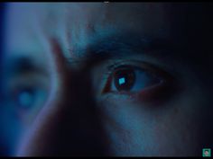 a man's eyes are glowing blue in the dark, with only one eye visible