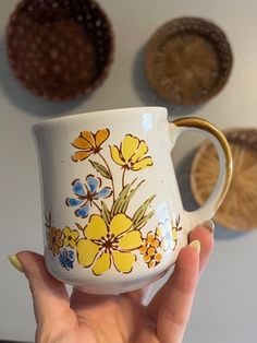 a hand holding a yellow and blue flowered coffee cup in front of some wall hangings