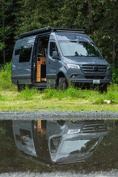 a van with its door open sitting in the grass next to a body of water