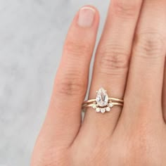 a woman's hand wearing a gold ring with a pear shaped diamond on it