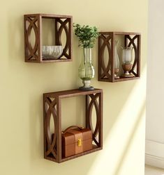 three wooden wall shelves with vases and other items on them against a yellow wall