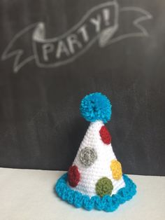 a crocheted party hat sitting on top of a white table next to a chalkboard