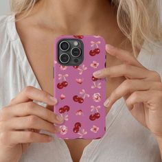 a woman holding up her phone case with cherries and flowers on the back in pink