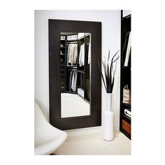 a mirror that is on the wall above a shelf with some clothes and a vase