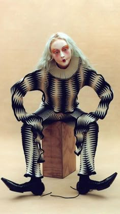 a woman sitting on top of a wooden block wearing black and white striped clothes with her hands in her pockets