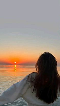 a woman is standing on the beach watching the sun go down