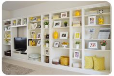 a living room filled with lots of white bookshelves covered in yellow and white pictures