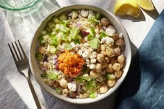 a white bowl filled with food next to a fork and lemon wedged in it