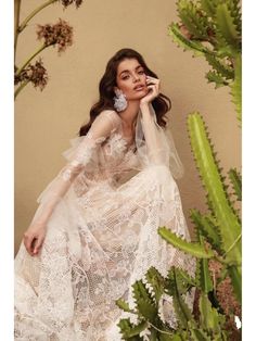 a woman in a white dress sitting next to a cactus