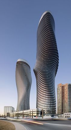 two very tall buildings sitting next to each other on the side of a road in front of tall buildings